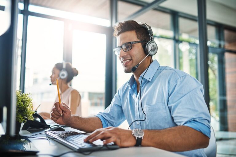 Sie haben die Antworten, nach denen Sie suchen. Ausschnitt eines gut aussehenden jungen Mannes, der in einem Callcenter arbeitet, mit einer weiblichen Kollegin im Hintergrund.