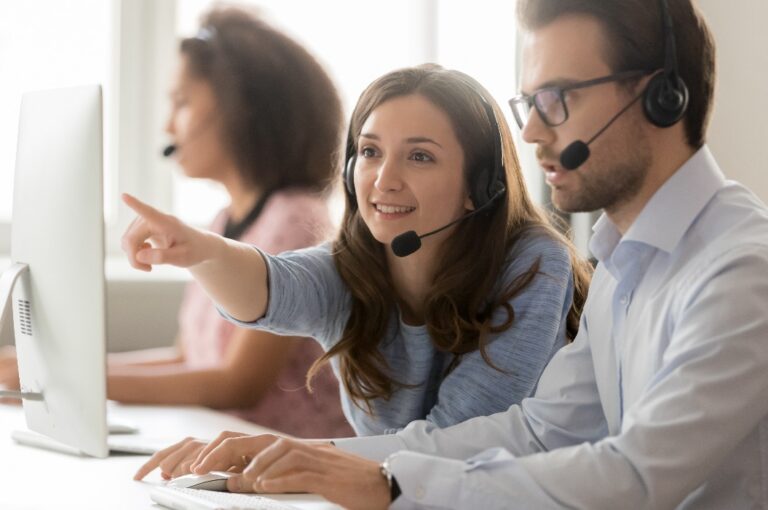Weiblicher Callcenter-Agent hilft männlichem Kollegen, der auf den Computer zeigt